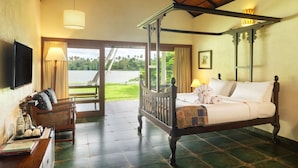 A four-poster bed with a view of a lake, a wicker chair, and a television on the wall. - Cranganor History Cafe Riverside Chateau (North Paravur)