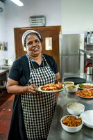 A person in a kitchen holding a plate of food, with various dishes and kitchen equipment in the background.