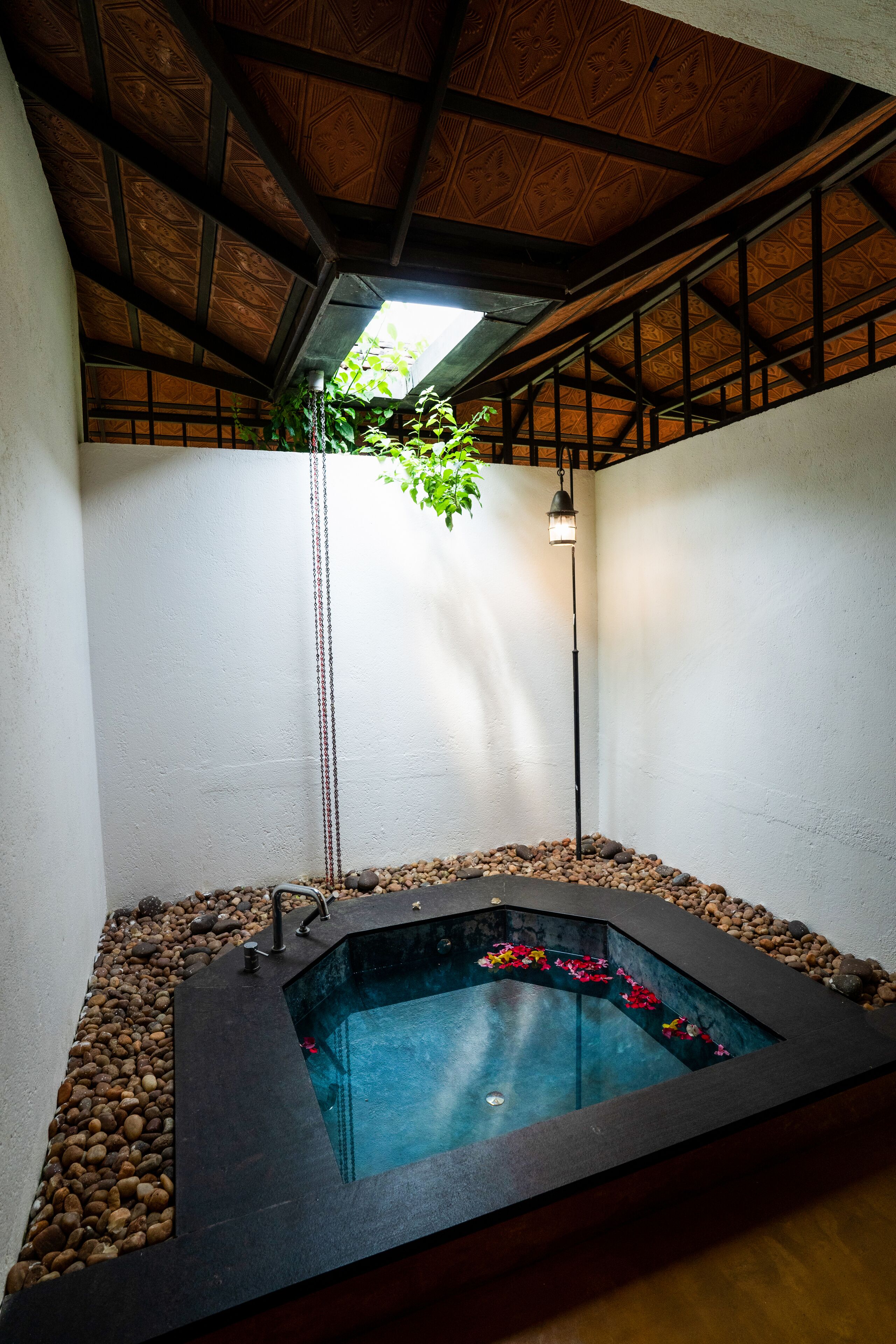 A spa area with a hot tub, surrounded by pebbles, under a wooden ceiling with a hanging light fixture.