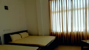 Una habitación de hotel con dos camas, una mesita y un ventanal con cortinas.