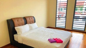 A neatly made bed with white linens and two towels, a dark headboard, and wooden flooring.
