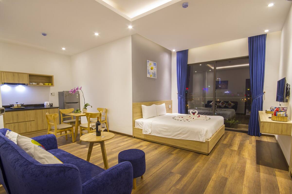 Una habitación de hotel moderna con cama, sofá, mesa de comedor y zona de cocina.