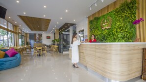A modern reception area with a wooden counter, a green wall with plants, and a blue sofa. - King House Villa Hotel (Da Nang)