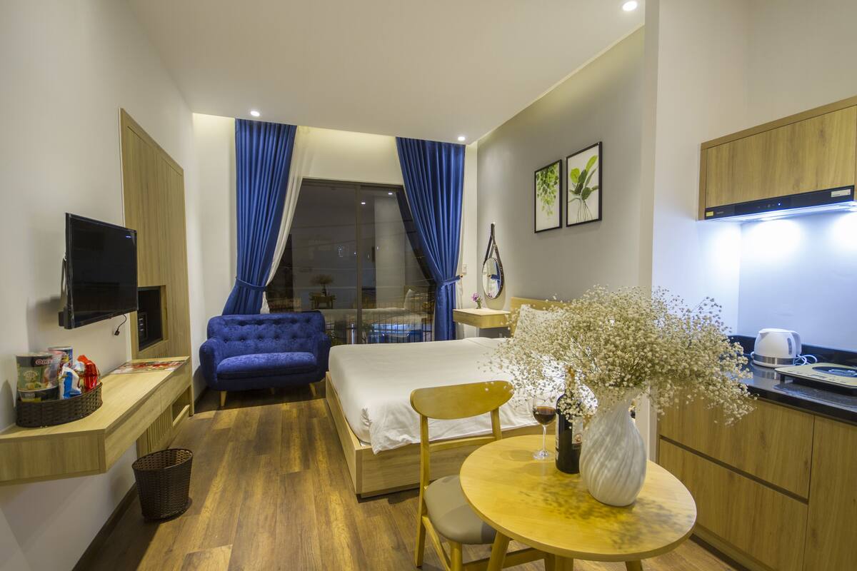 Una habitación de hotel moderna con una cama, un escritorio con computadora, una silla, una mesita con un florero y vistas al exterior.