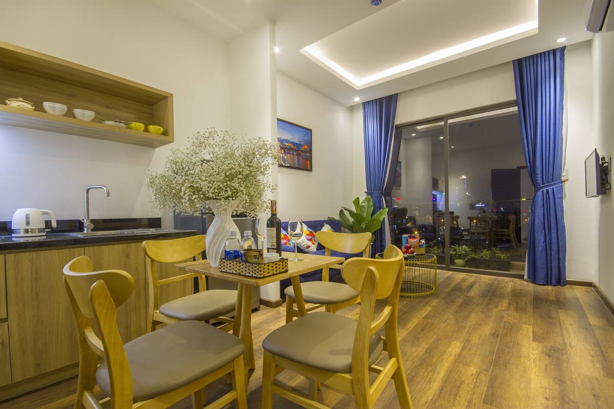 Una cocina moderna con armarios de madera, una zona de comedor con sillas de madera, un florero con flores y vistas a la ciudad a través de la puerta de cristal.