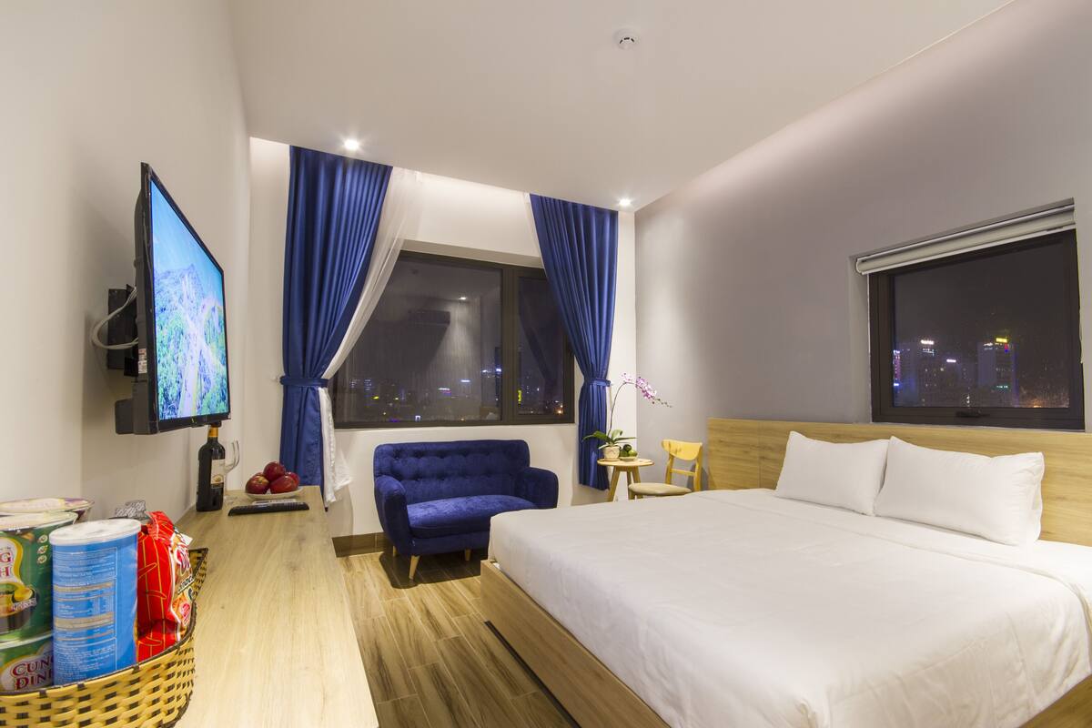 Habitación de hotel con cama, televisión, ventana con cortinas, una mesita con una planta y una silla.