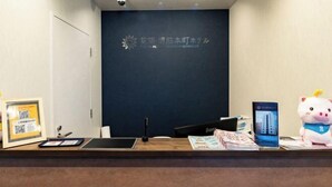 A reception desk with a dark blue wall, a framed sign, a tablet, a smartphone, and a plush toy. - Floral Hotel · SakaisuJi-Honmachi Osaka (Osaka)