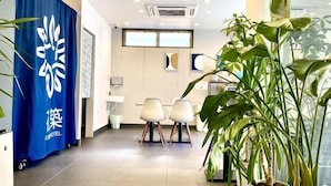 A hotel reception area with a blue curtain, two white chairs, and a large potted plant. - Floral Hotel · SakaisuJi-Honmachi Osaka (Osaka)