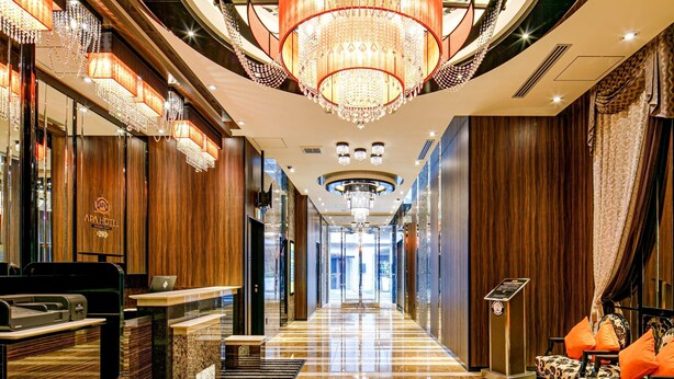 Un vestíbulo de hotel con suelo de mármol, paneles de madera, un mostrador de recepción y una araña.