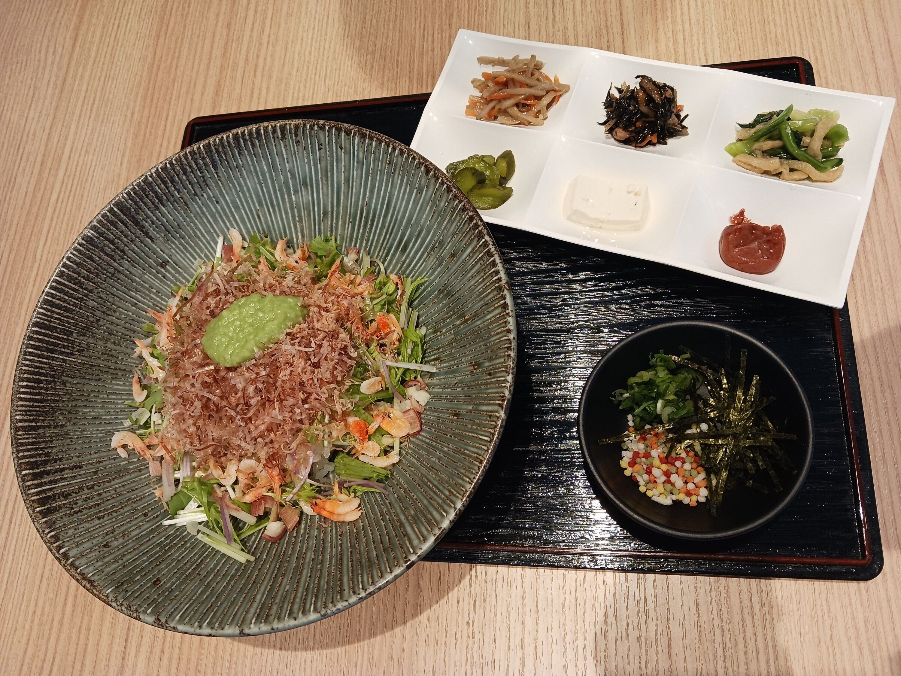 A plate of food with various side dishes on a black tray.