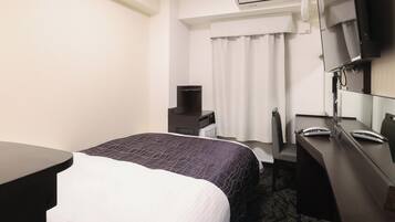 Habitación de hotel con cama, escritorio, silla, televisor y aire acondicionado.