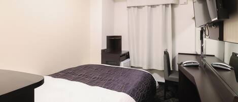 A hotel room with a bed, a desk, a chair, a TV, and an air conditioning unit.