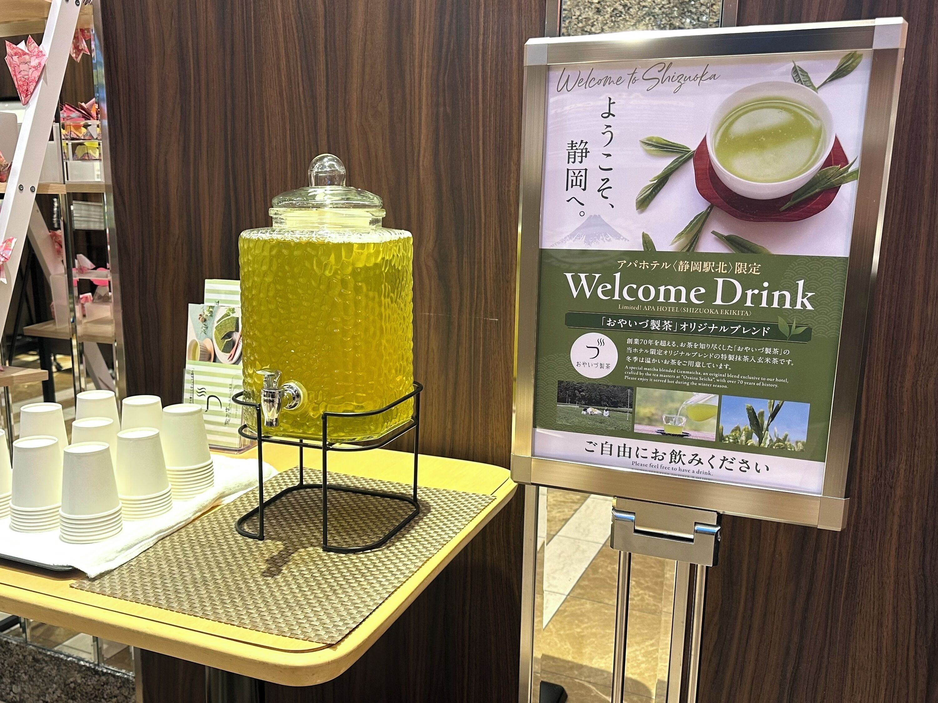 A welcome drink station with a large dispenser and cups, and a signboard with Japanese text.