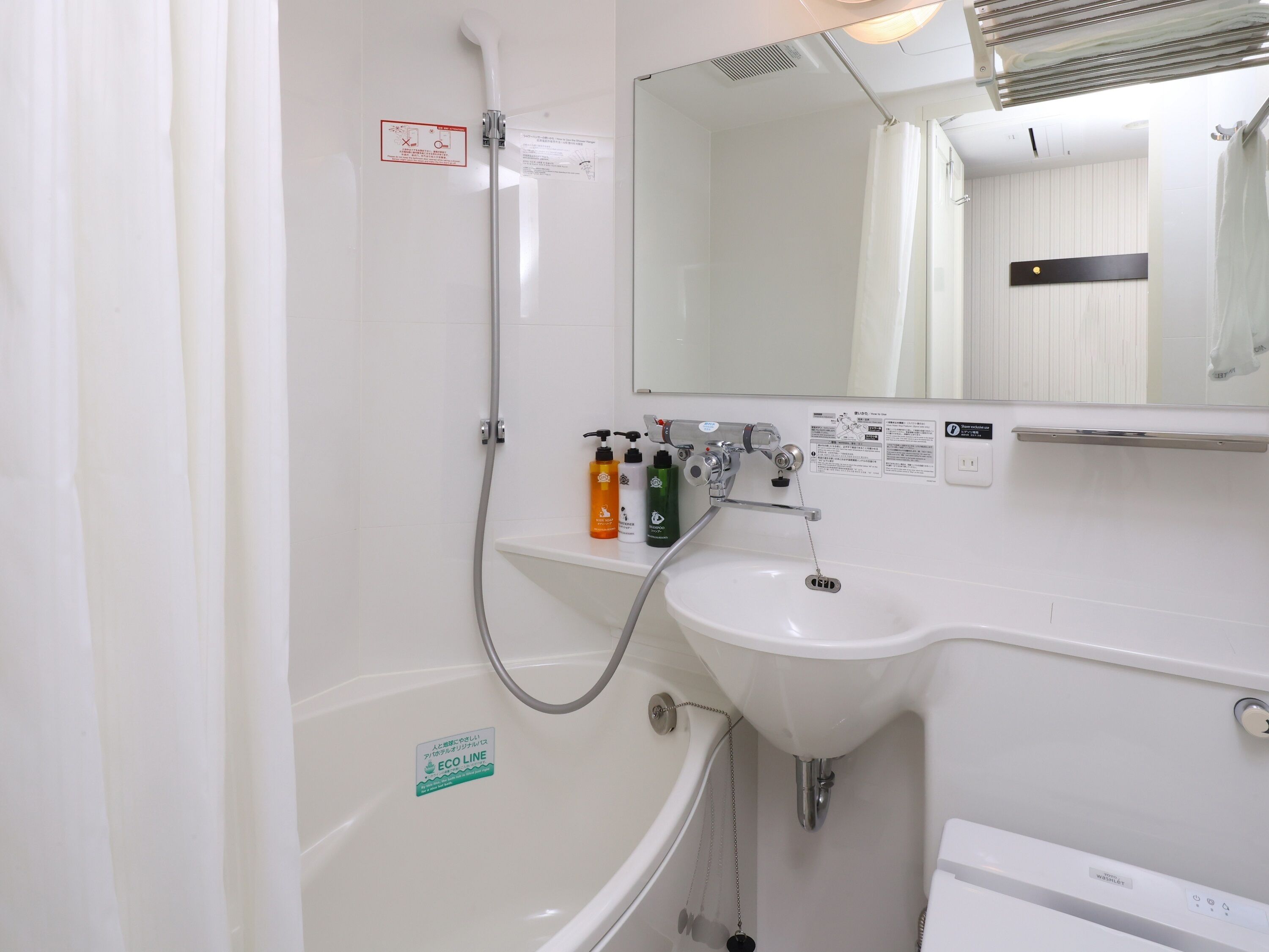 Een badkamer met een bad, een wastafel en een douche. Er staan toiletartikelen op de wastafel en een bordje dat wijst op een milieuvriendelijk watersysteem.