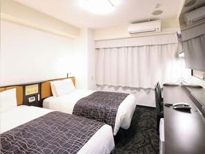 Two single beds with patterned bedspreads, a flat-screen TV, and a desk with a telephone.