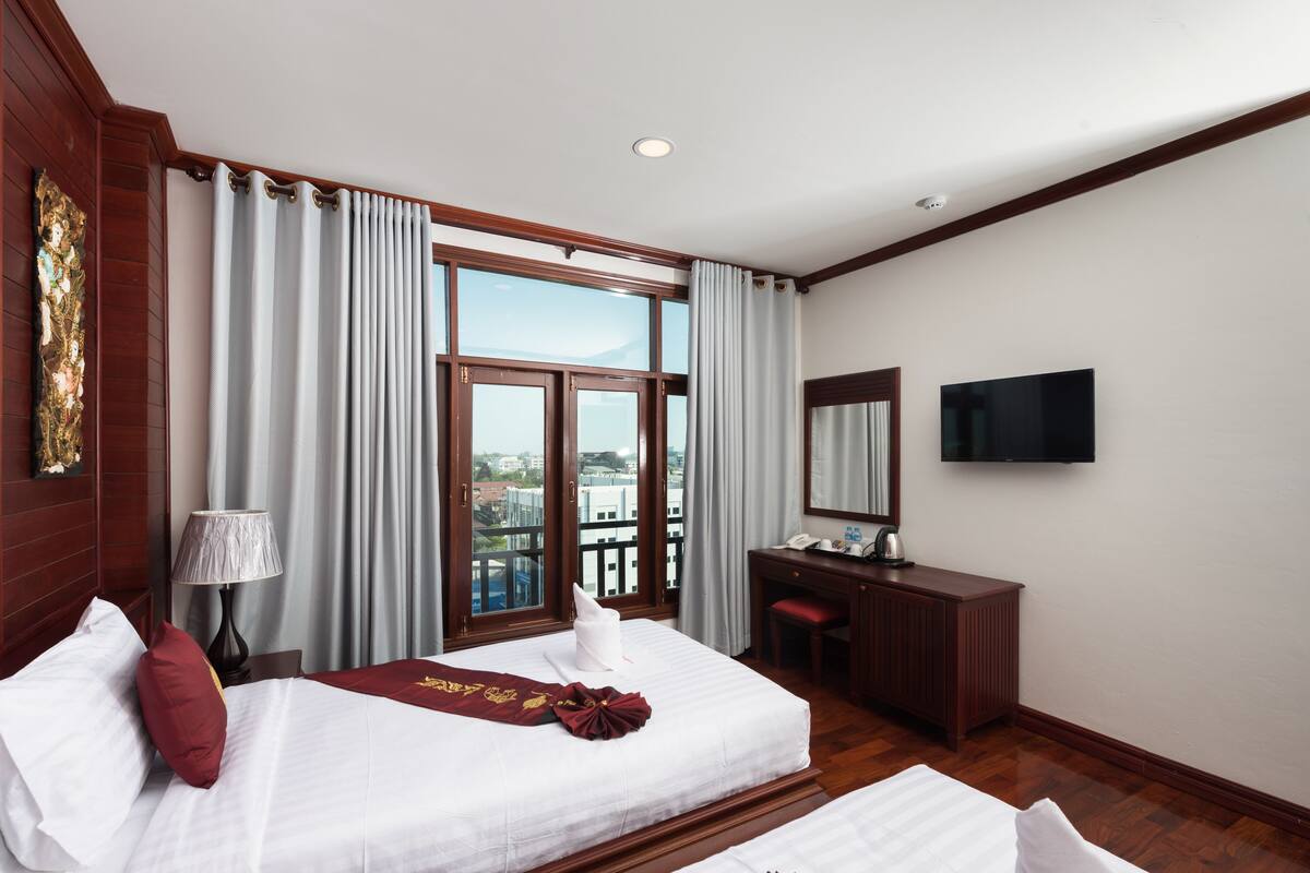 A hotel room with a bed, a desk, a chair, a TV, and a window with curtains.