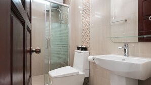 A modern bathroom with a glass shower enclosure, a white toilet, and a sink with a glass shelf. - Manorom Chateau Hotel (Vientiane)