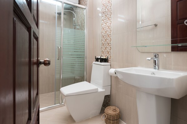 A modern bathroom with a glass shower enclosure, a white toilet, and a sink with a glass shelf. - Manorom Chateau Hotel (Vientiane)