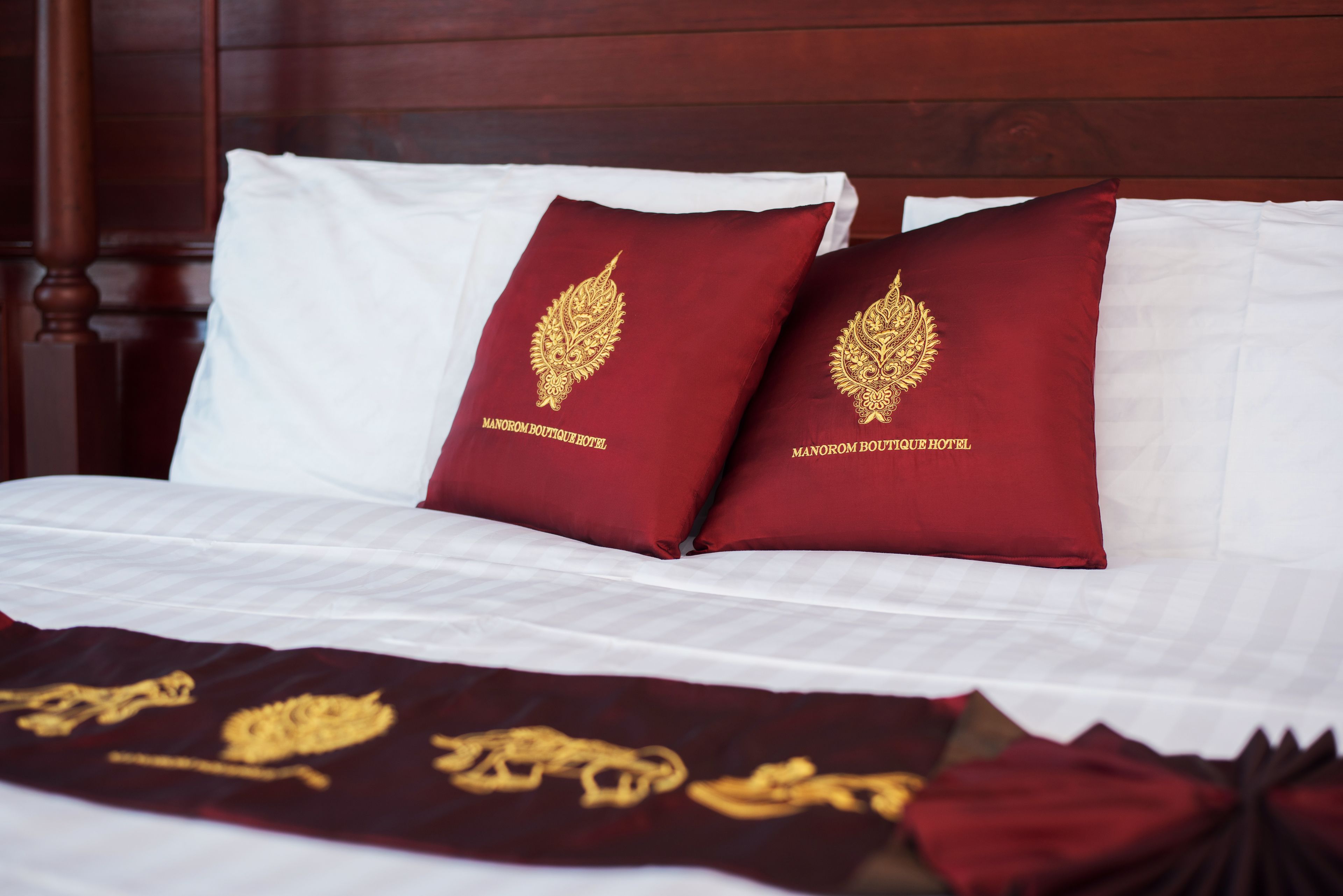 A bed with white linens and two red pillows with gold embroidery.