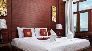 A hotel room with a large bed, wooden panel walls, and a view of the city through the window. - Manorom Chateau Hotel (Vientiane)