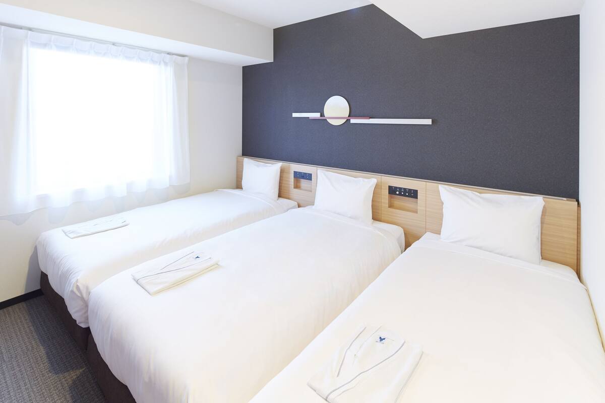 Una habitación de hotel con dos camas, un reloj de pared moderno y una ventana con cortinas translúcidas.