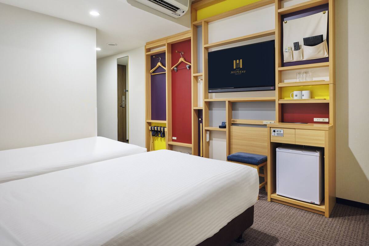 Habitación de hotel con cama, armario con varios compartimentos, televisión y un refrigerador pequeño.