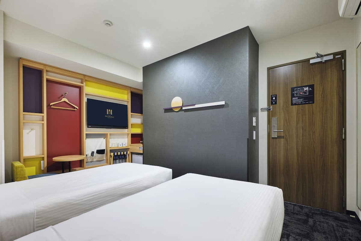 Habitación de hotel con dos camas, un escritorio, un armario y una puerta con un cartel.
