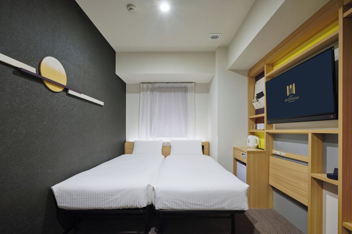 Una cama doble con cabecera, una mesita de noche pequeña, un televisor y una estantería con objetos.