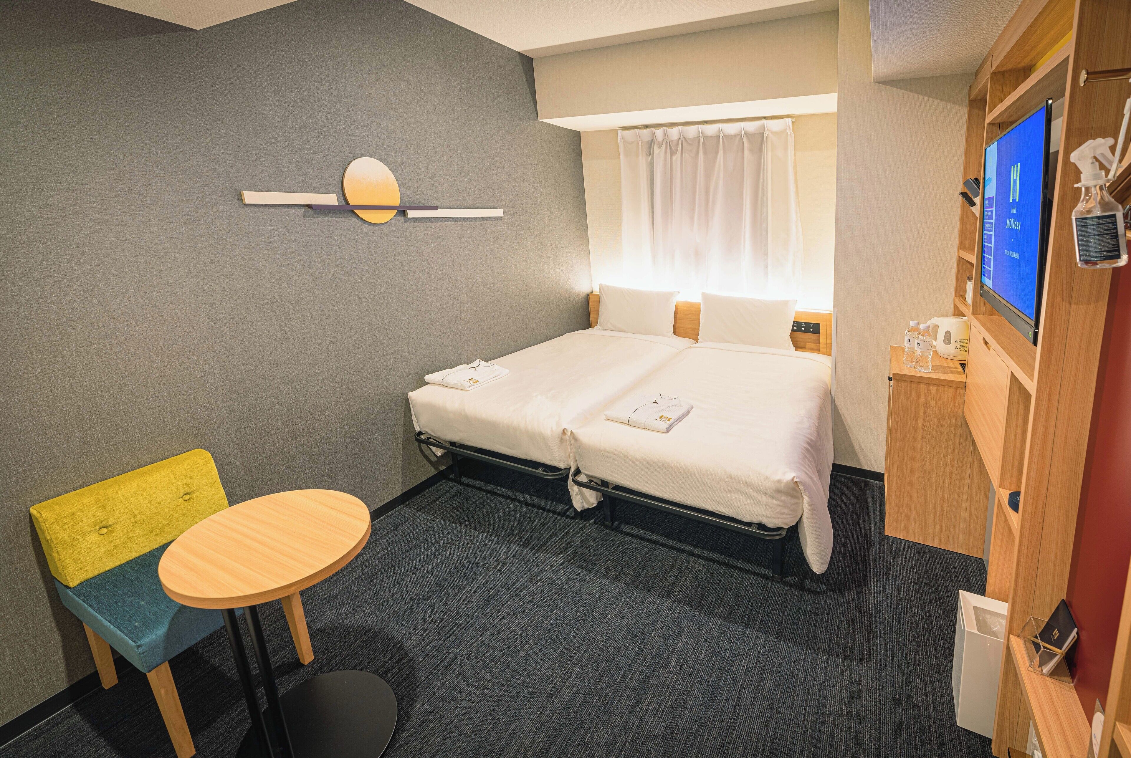 A hotel room with a bed, a small table, a chair, a TV, and a bathroom area.