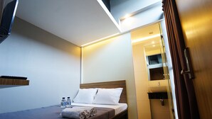A modern hotel room with a single bed, a small bedside table with water bottles, a wooden headboard, and a built-in TV. - The Lively Hotel Kualanamu Airport Medan (Medan)