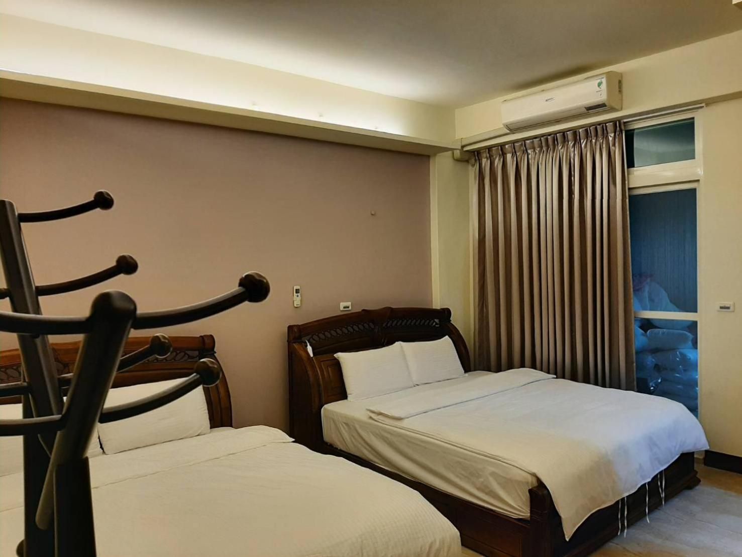 Habitación de hotel con dos camas, cabecero de madera, ventana con cortinas y equipo de aire acondicionado.
