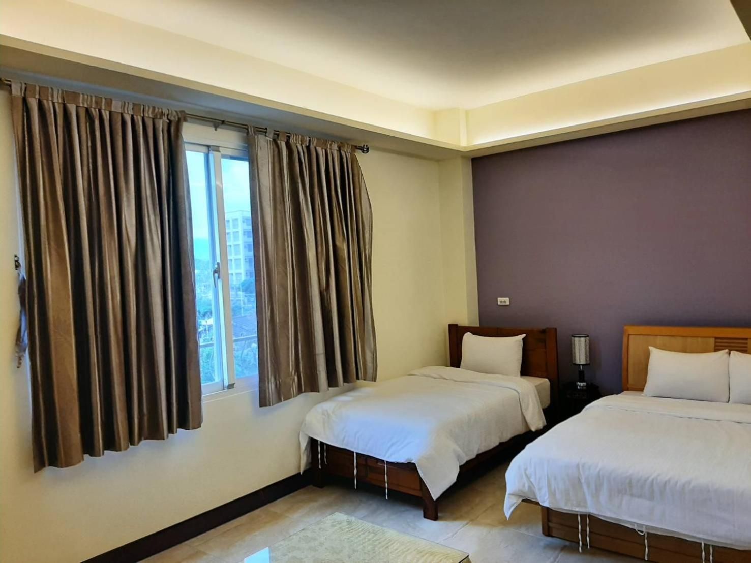 A hotel room with two beds, a window with curtains, a nightstand, and a lamp.