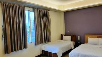 A hotel room with two beds, a window with curtains, a nightstand, and a lamp.