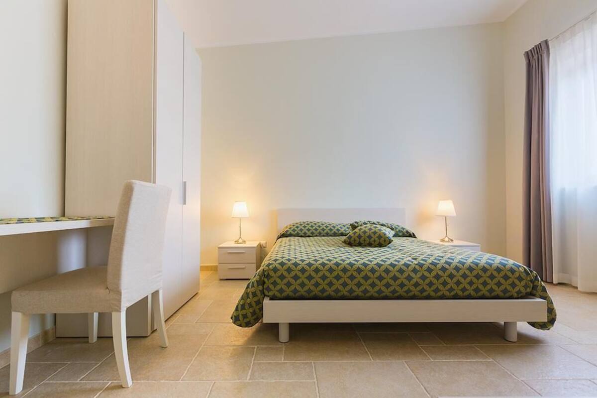 Ein Schlafzimmer mit einem Bett, zwei Nachttischen, einem Sessel und einem Schreibtisch.