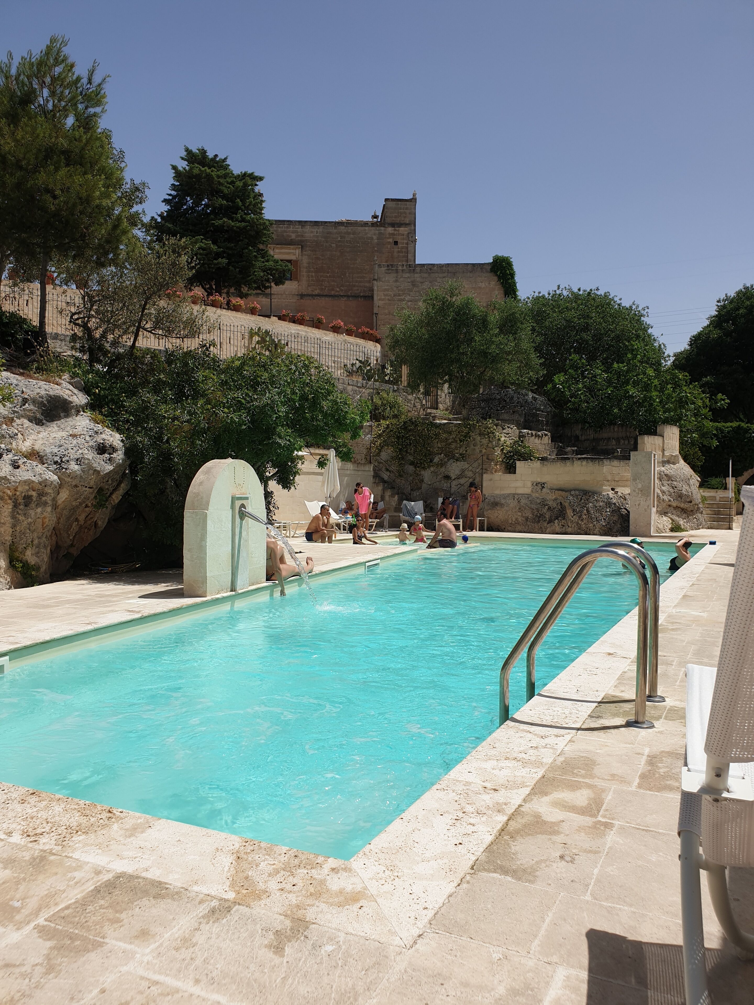 A swimming pool with clear water, surrounded by stone tiles and a stone wall in the background.