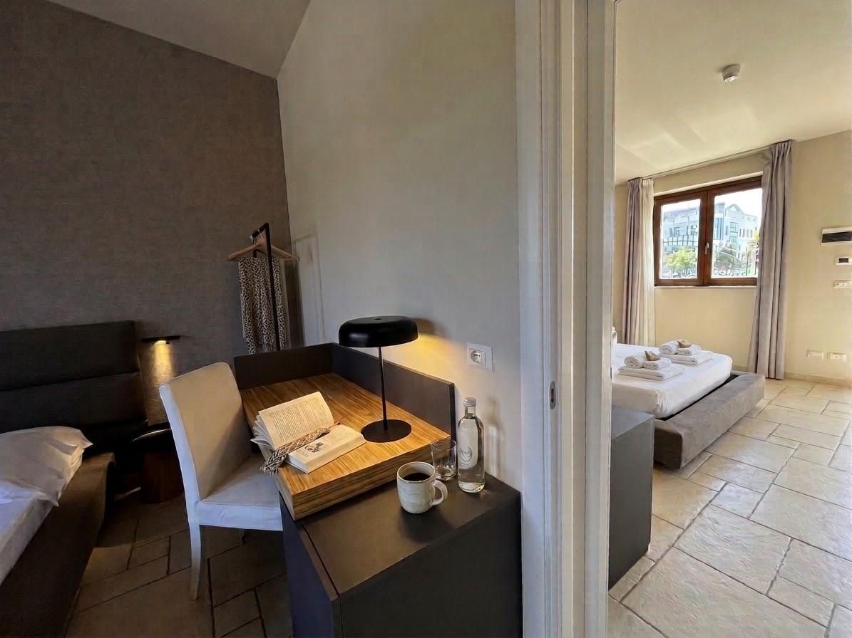 Une chambre d’hôtel comprenant un lit, un bureau avec une chaise, une table de chevet avec une lampe, une fenêtre avec des rideaux et une vue sur l’extérieur.