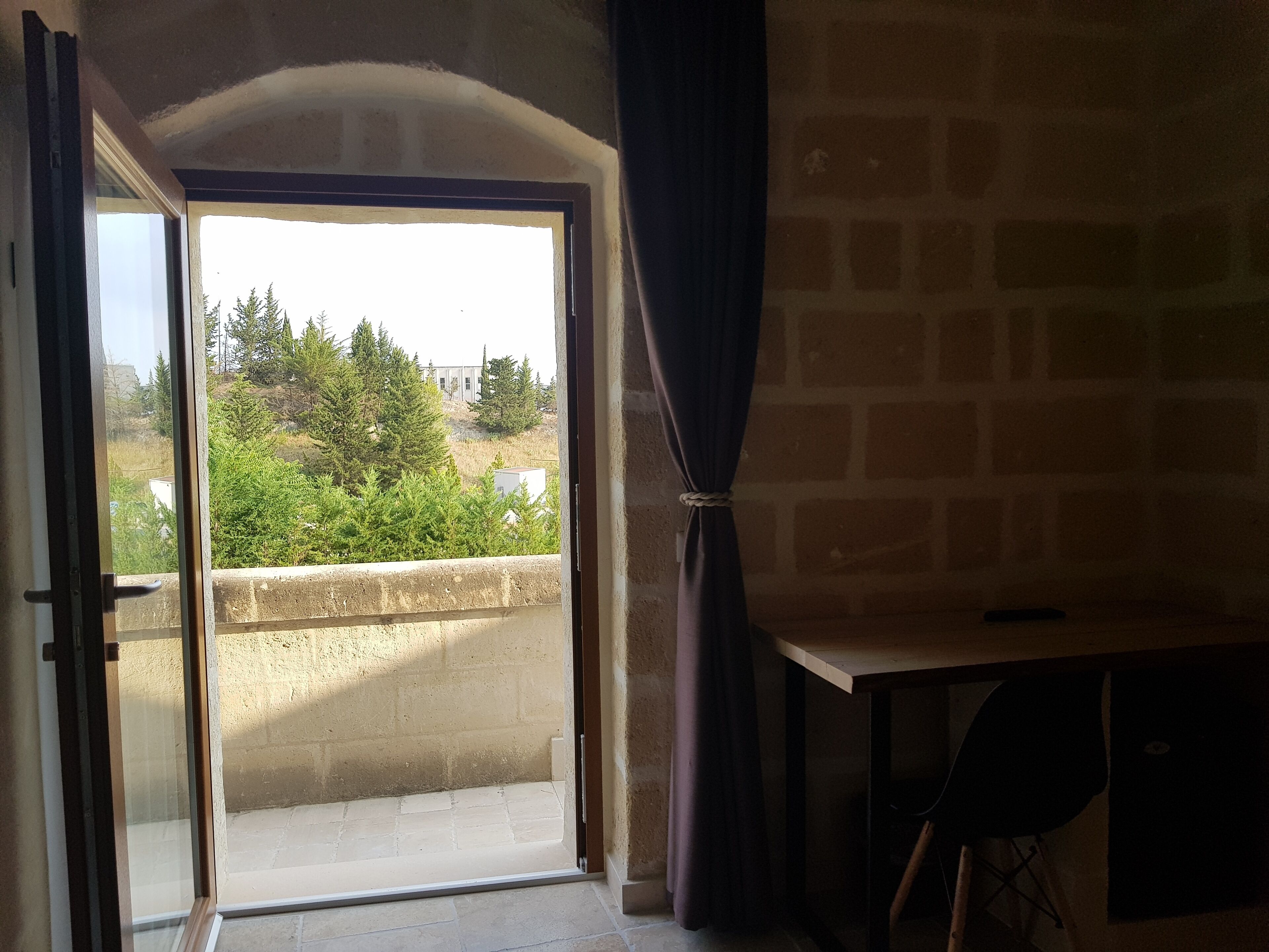 Une porte ouverte donnant sur un balcon d’où l’on peut admirer les arbres et les bâtiments.