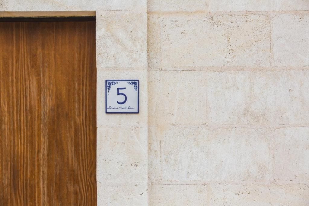 A door with a number plaque indicating '5' and a partial view of a stone wall.