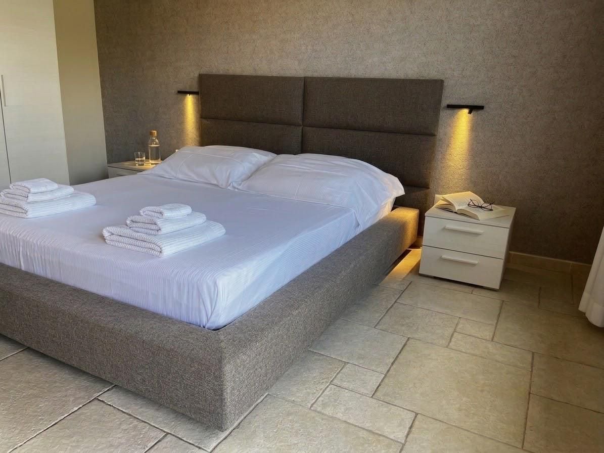 A neatly made bed with folded towels, a bedside table with a lamp, and a nightstand with a glass of water.