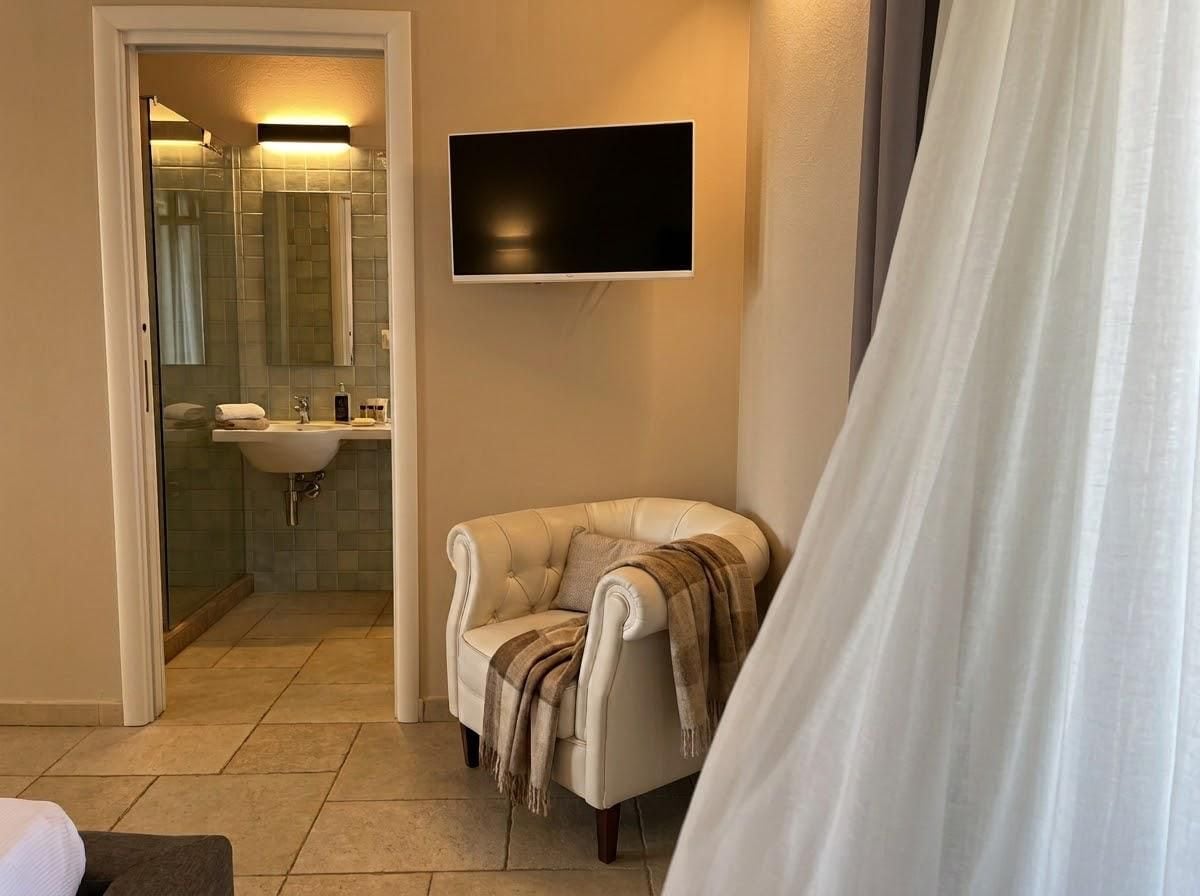 A bathroom with a shower, a sink, a television mounted on the wall, and a chair with a blanket.