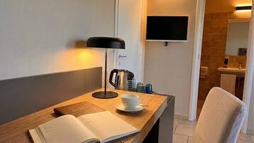 Una habitación moderna con un escritorio de madera, un libro abierto, una taza, una lámpara y un televisor montado en la pared.