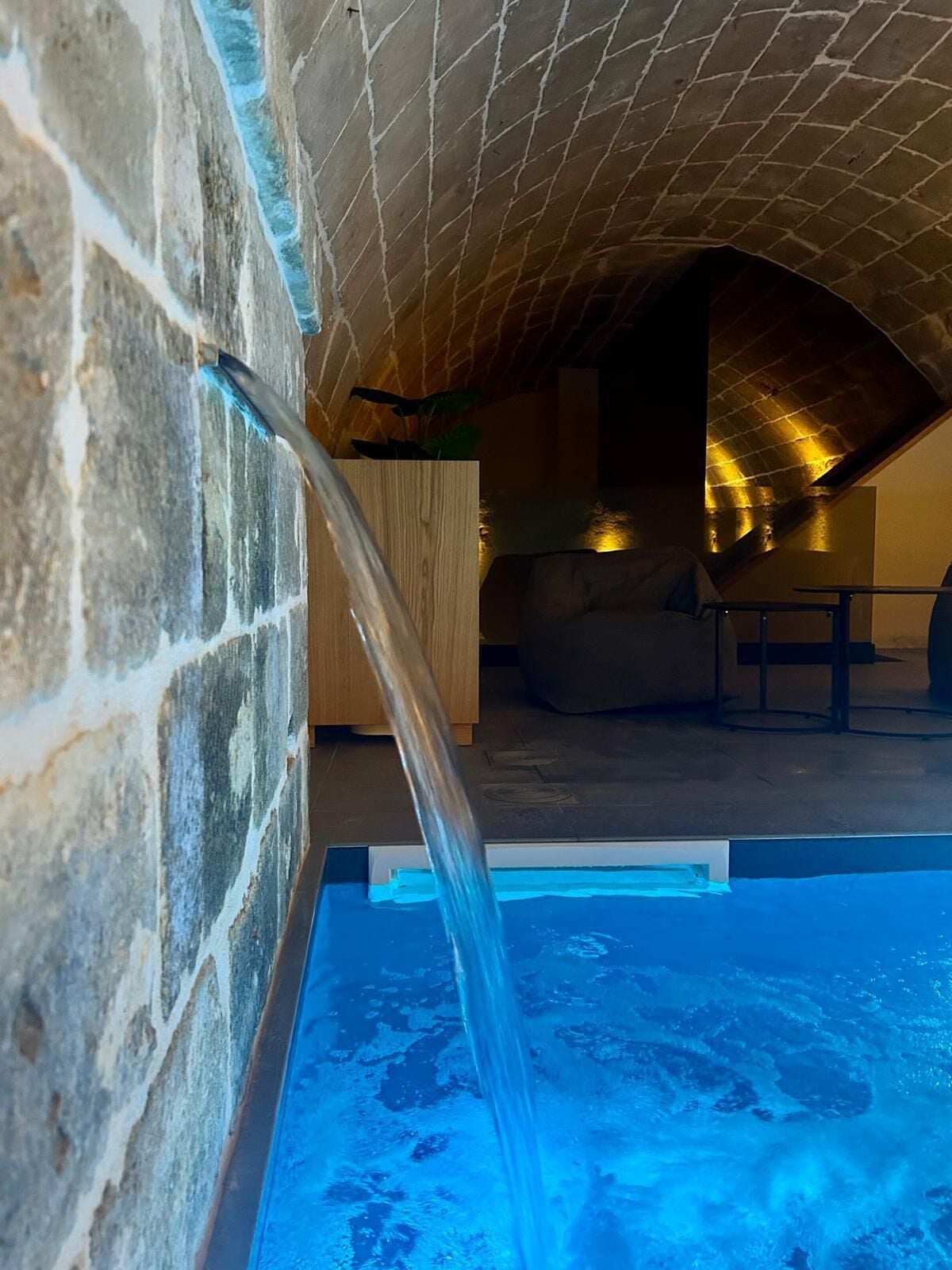 A stone-walled indoor pool with a clear water feature.