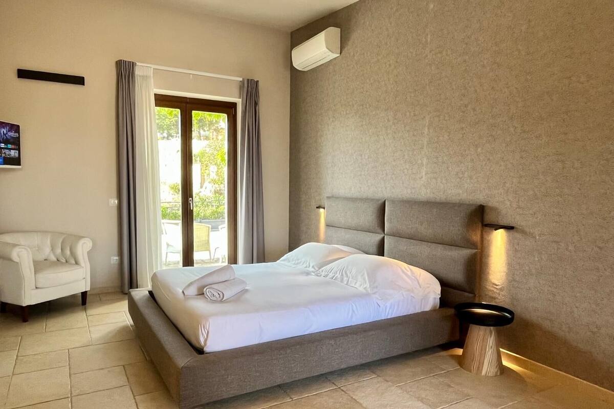 Ein modernes Hotelzimmer mit einem großen Bett, einer Couch, einem Fernseher und einer Glastür zum Außenbereich.