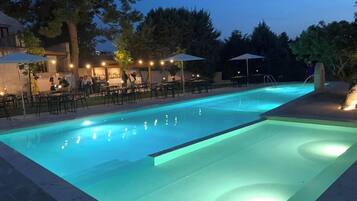 Ein Schwimmbecken mit gefliestem Sonnendeck, umgeben von Gartenmöbeln und Sonnenschirmen.