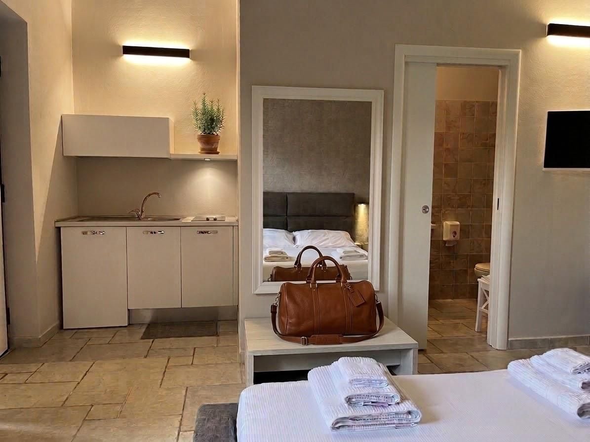 Habitación de hotel con una cama, un escritorio con un bolso, un espejo, un lavamanos y un taburete pequeño.