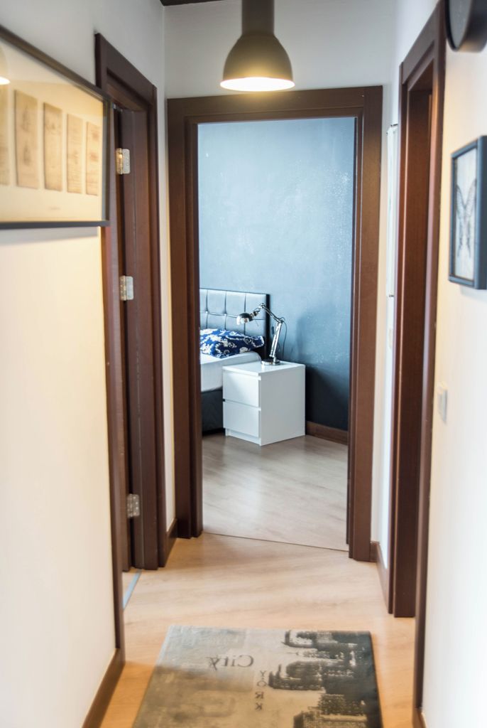A hallway leading to a bedroom with a bed, bedside table, and a hanging lamp.