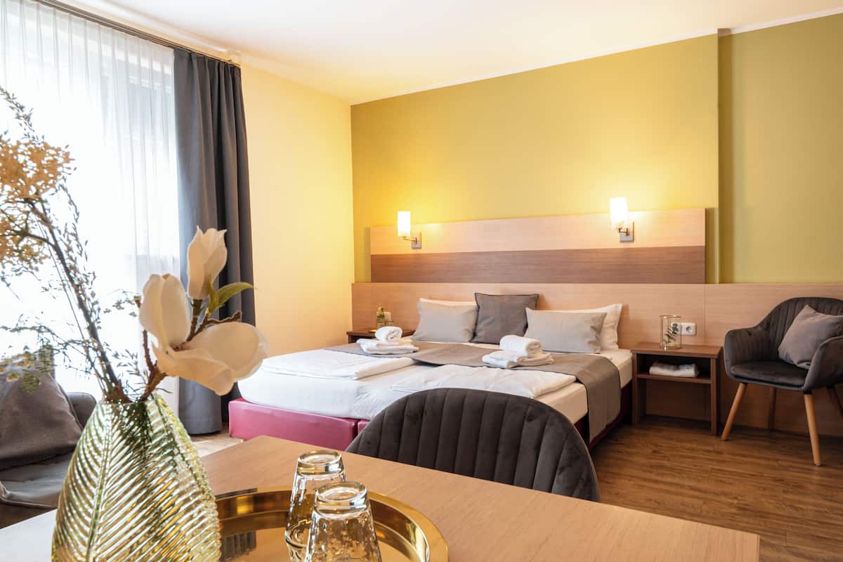 Une chambre d’hôtel comprenant un lit, des tables de chevet, un bureau, une chaise et un vase avec des fleurs.