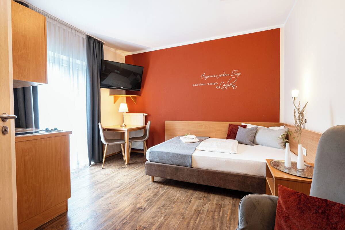 Une chambre d’hôtel équipée d’un lit, d’un bureau, d’une télévision et d’un mur orné d’une citation inspirante.