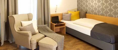 A hotel room with a bed, a desk with a laptop, a chair, and a TV mounted on the wall.