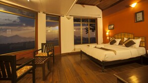 A bedroom with a large bed, a wooden floor, a window with a mountain view, and a chair. - Edakkal Hermitage (Sulthan Bathery)